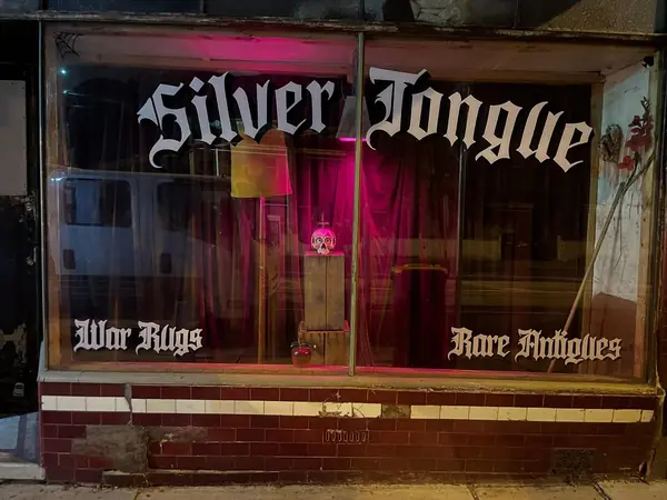 The Silver Tongue shop window at night, lettered War Rugs and Rare Antiques