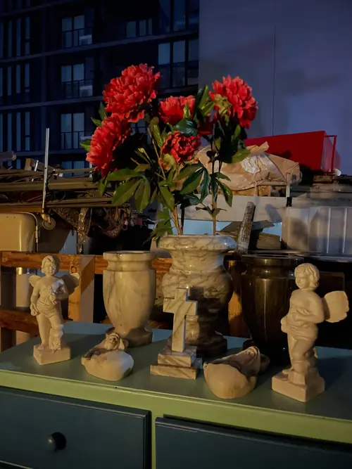 Red flowers, stone vases and small cherub statues on a shelf in the shop