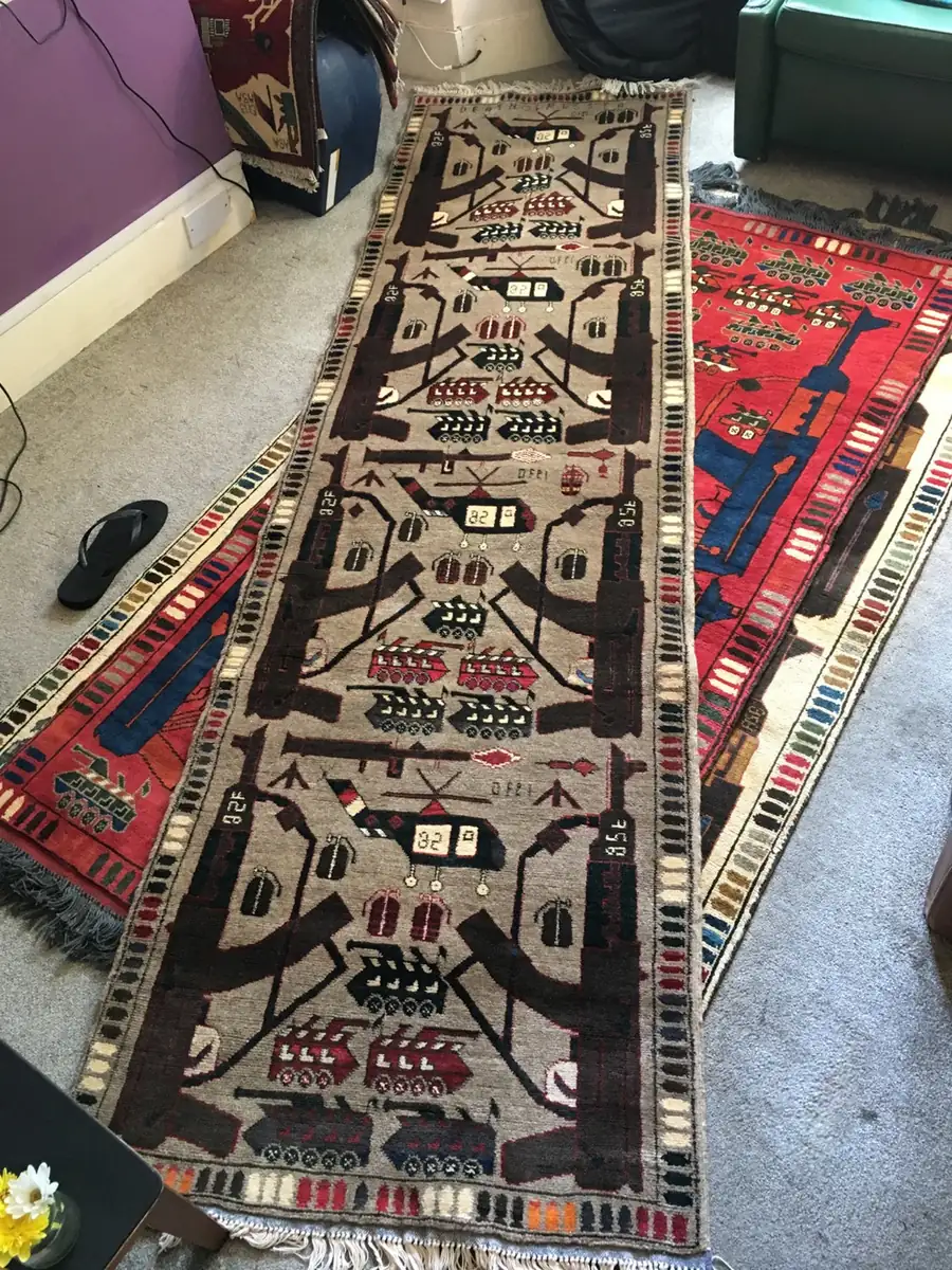 A grey Afghan war runner laid over a red war rug on the floor